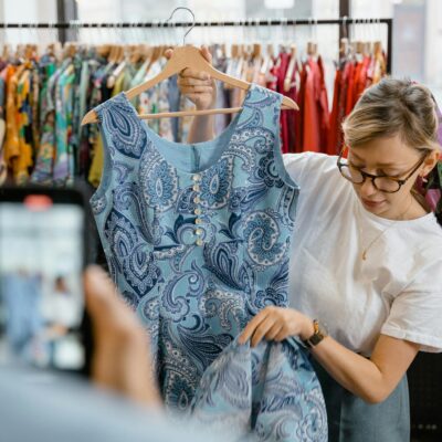 Woman inspecting a blue patterned dress in a retail clothing store. Fashion and shopping concept.